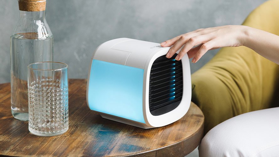 White air purifier with light blue glowing light on table next to glass and bottle