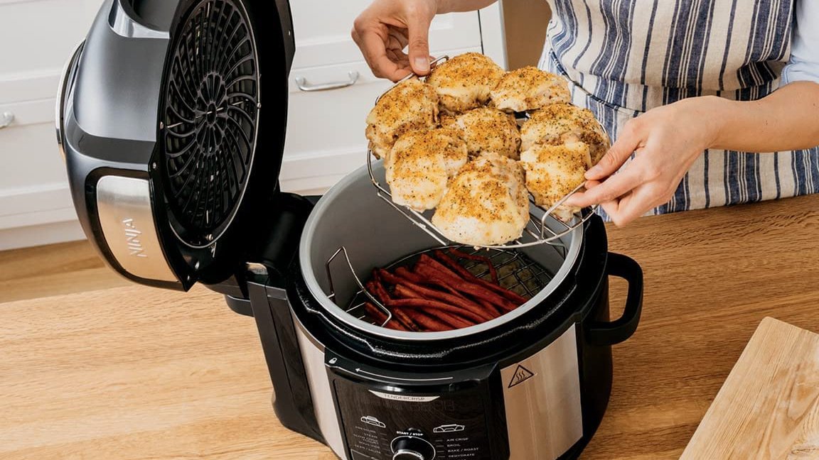 Hands lifting tray of chicken out from ninja 12-in-1, with carrots still inside