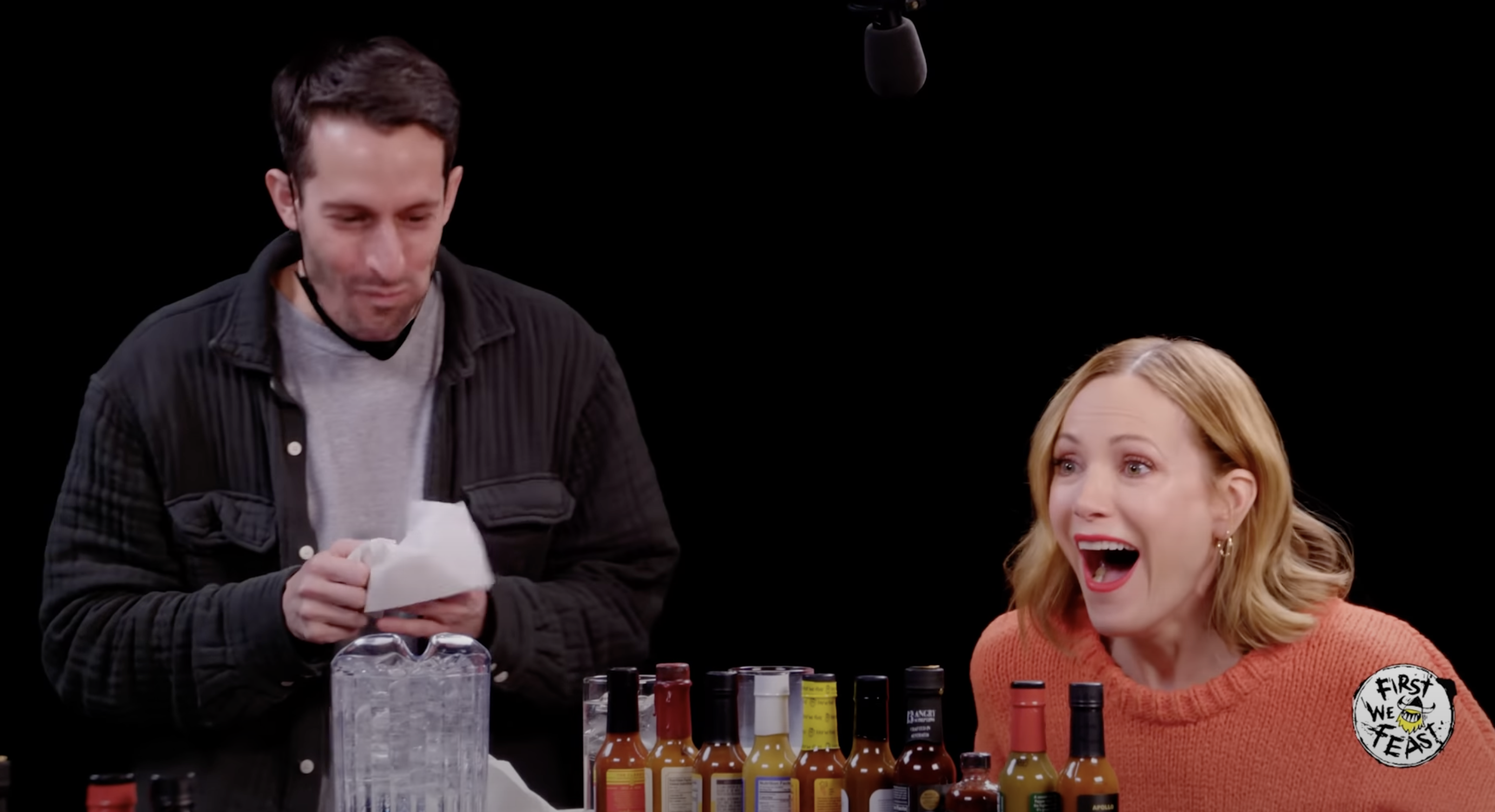 hot ones creator eating a very spicy wing while leslie mann laughs