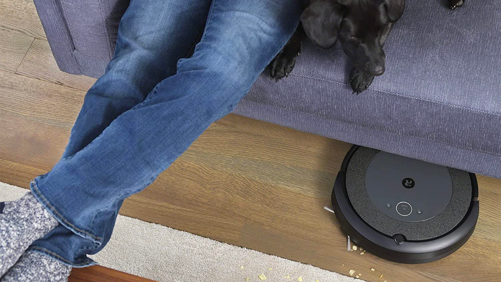 an irobot roomba i4 cleans under a couch that a dog and a person are sitting on
