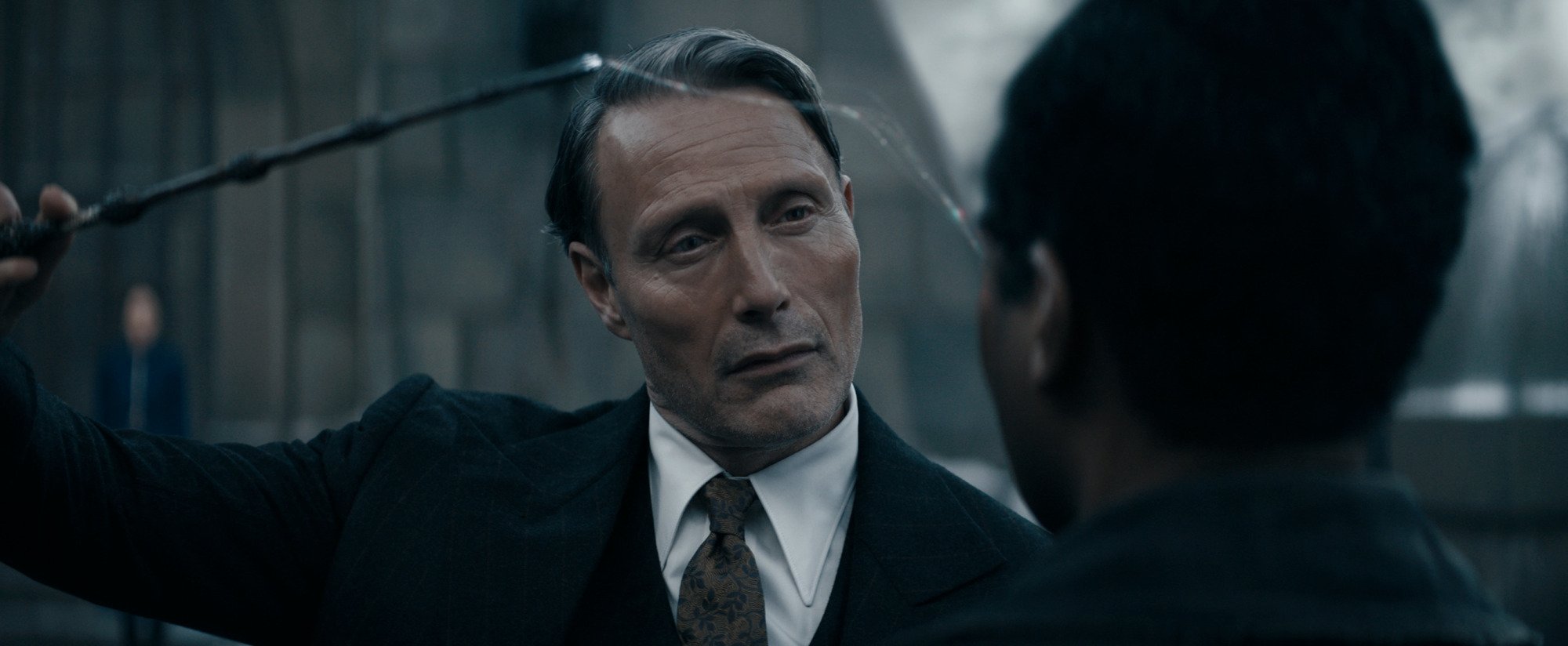 Film still of a man pointing his wand at another man; a silver strand of magic connects the end of the wand to the man's temple.