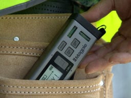 Hand pulling grey and black distance measurer out of tan back pocket