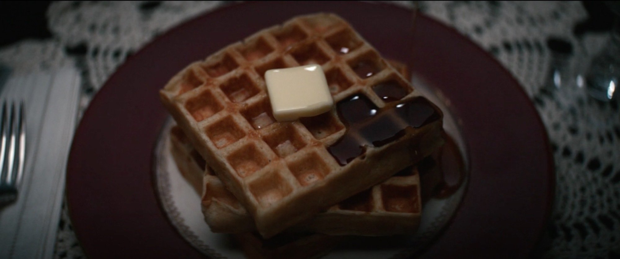 A stack of three waffles with a pat of butter and some syrup on top.