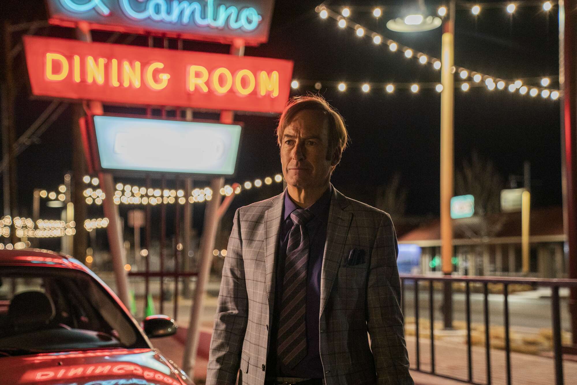 A man (Bob Odenkirk as Jimmy McGill on "Better Call Saul") standing outside in front of a neon sign that reads "El Camino Dining Room."
