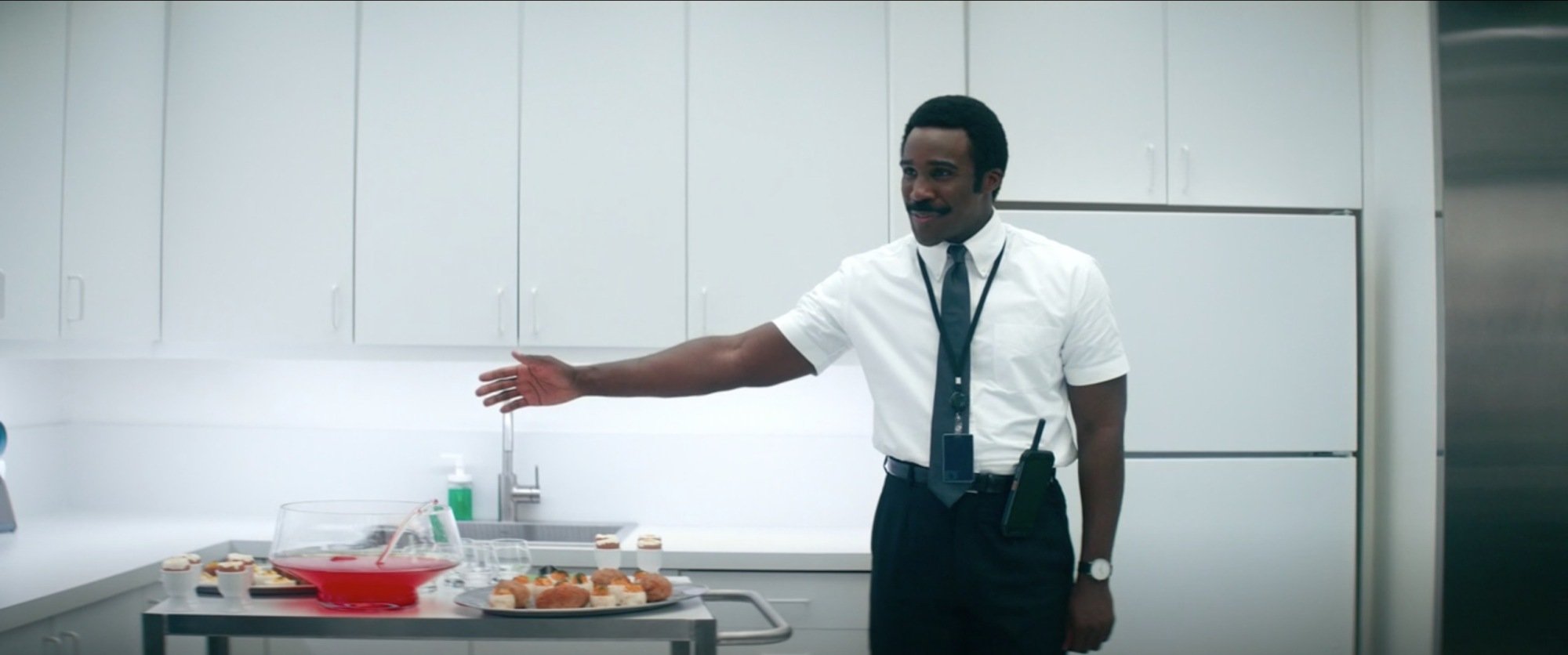 A man (Tramell Tillman as Mr. Milchick on "Severance") gesturing to a rolling cart that holds plates of deviled eggs. 