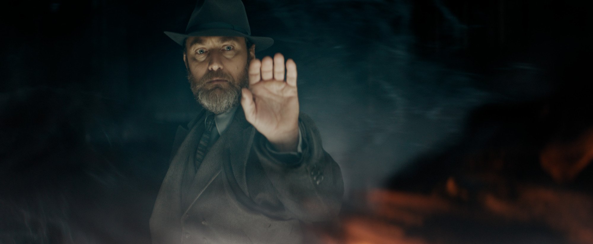 Film still of a bearded man holding out his hand toward a red cloud of magic.