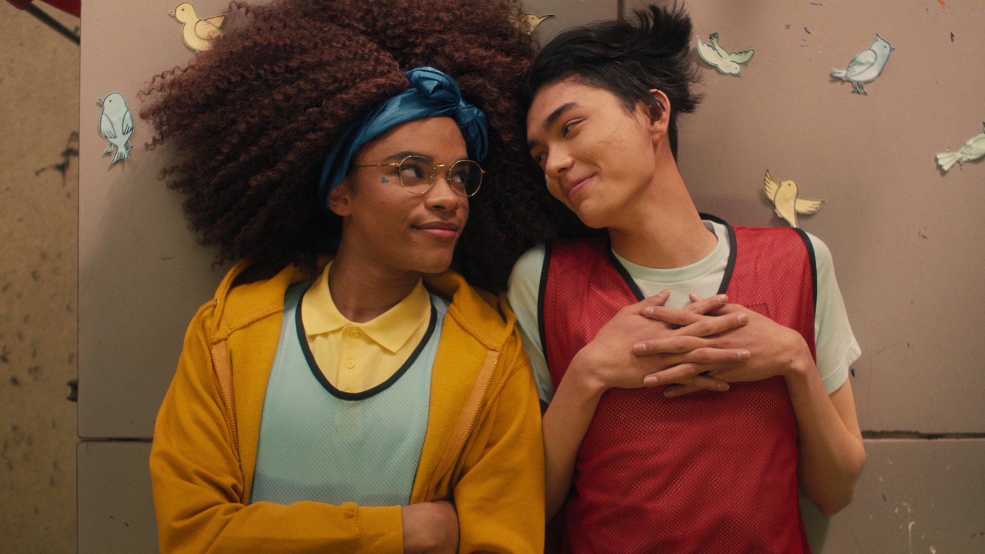 William Gao and Yasmin Finney look at each other as Tao and Elle in "Heartstopper" lying on a desk.