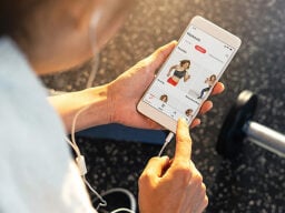 Person with earphones plugged into phone showing jillian michaels app with workout videos