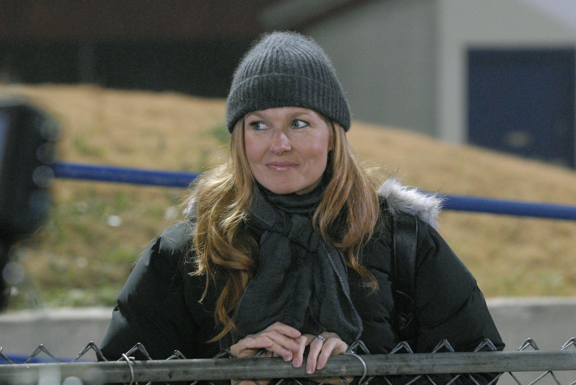A woman (Connie Britton as Tami Taylor on "FNL") standing against a fence.