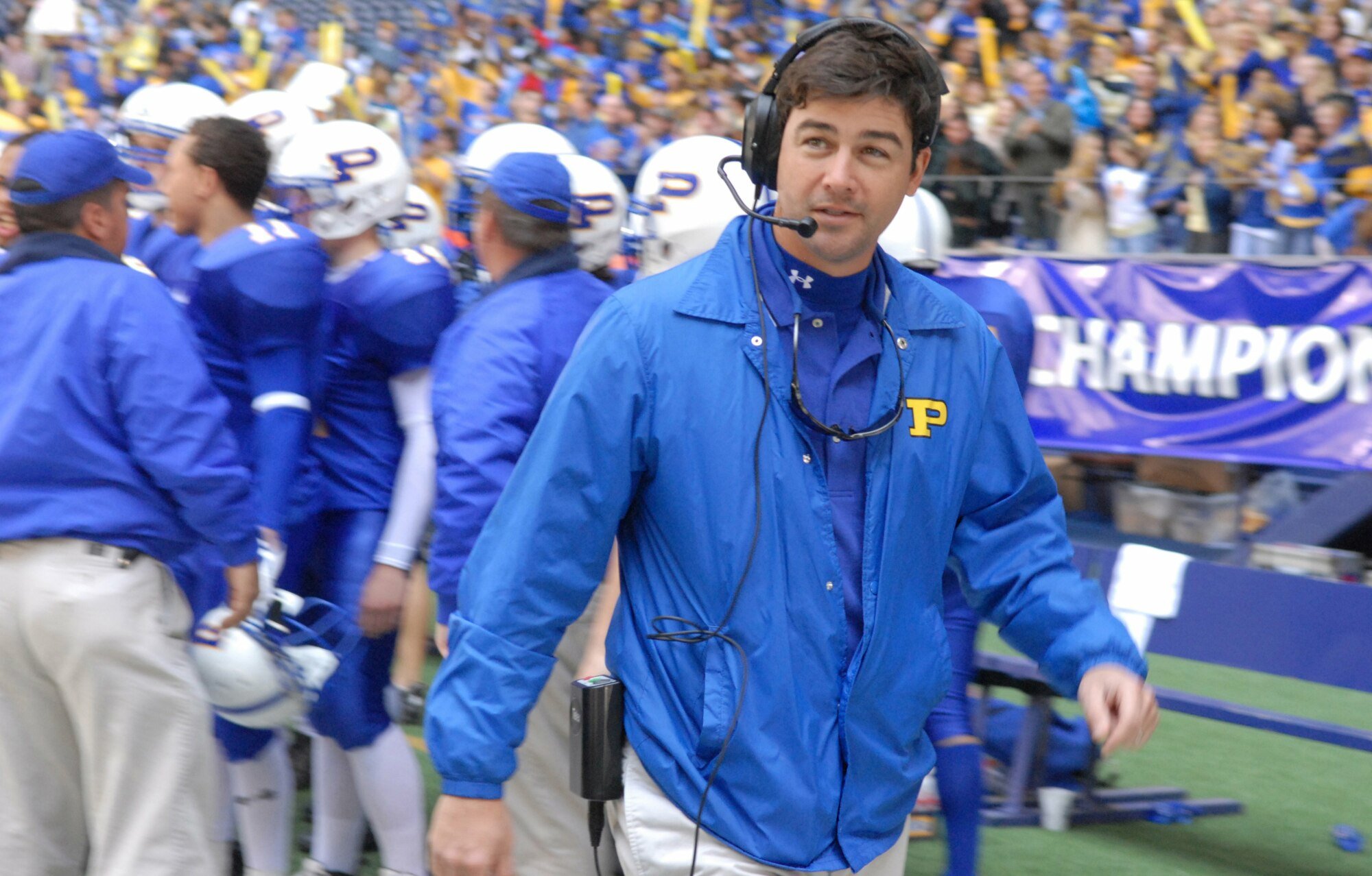 A football coach (Kyle Chandler as Coach Eric Taylor on "FNL") wearing a Panthers jacket on the field mid-game.