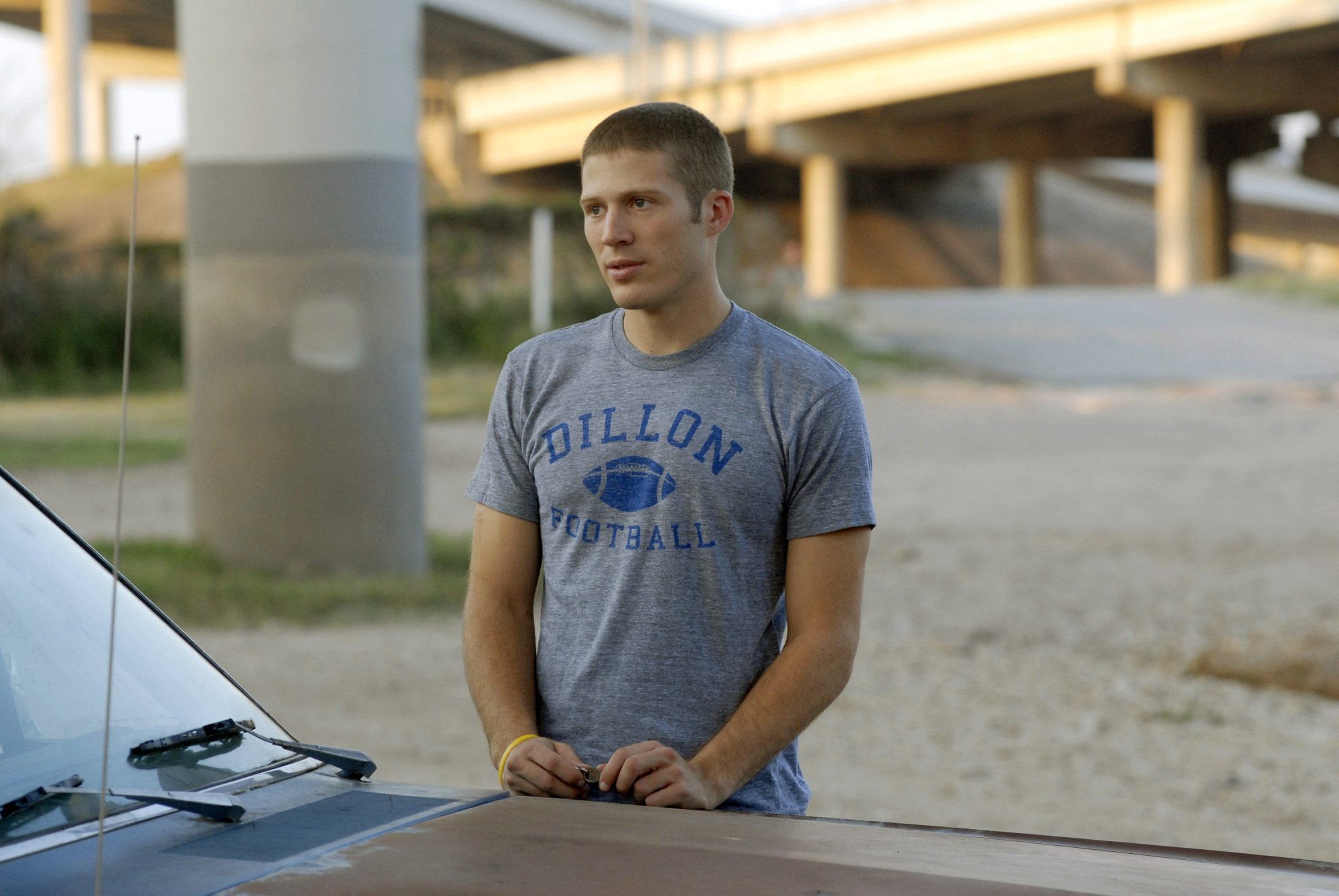 A teenage boy (Zach Gilford as Matt Saracen on "FNL") standing with his hands on a car.