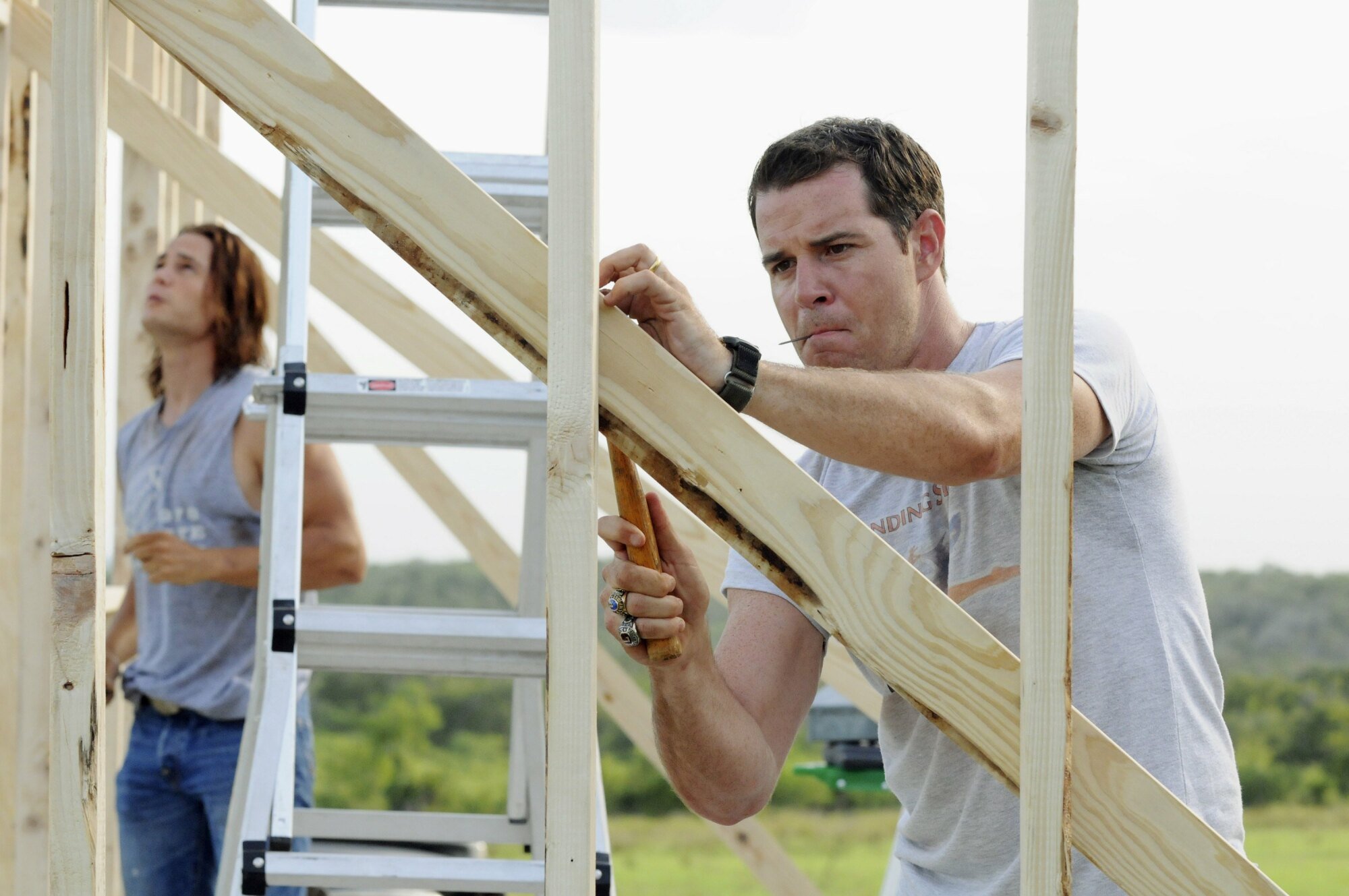 A man (Derek Phillips as Billy Riggins in "FNL") hammering a nail into a wooden beam.