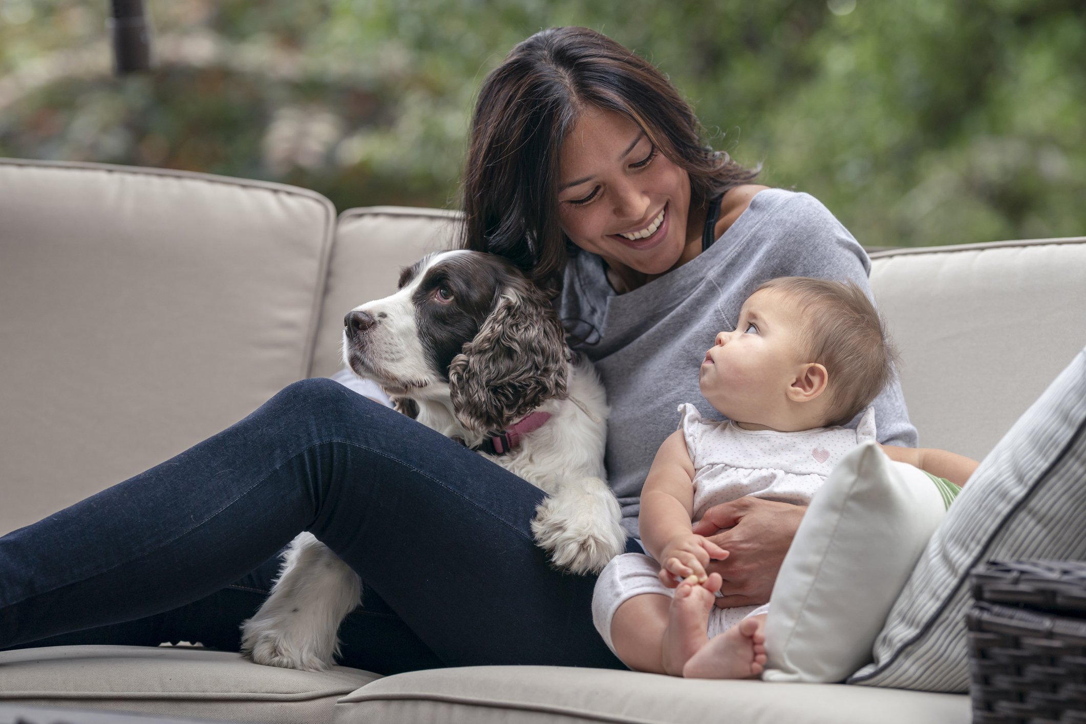 Image of woman on a couch holding her baby in one hand and a dog resting on her lap.