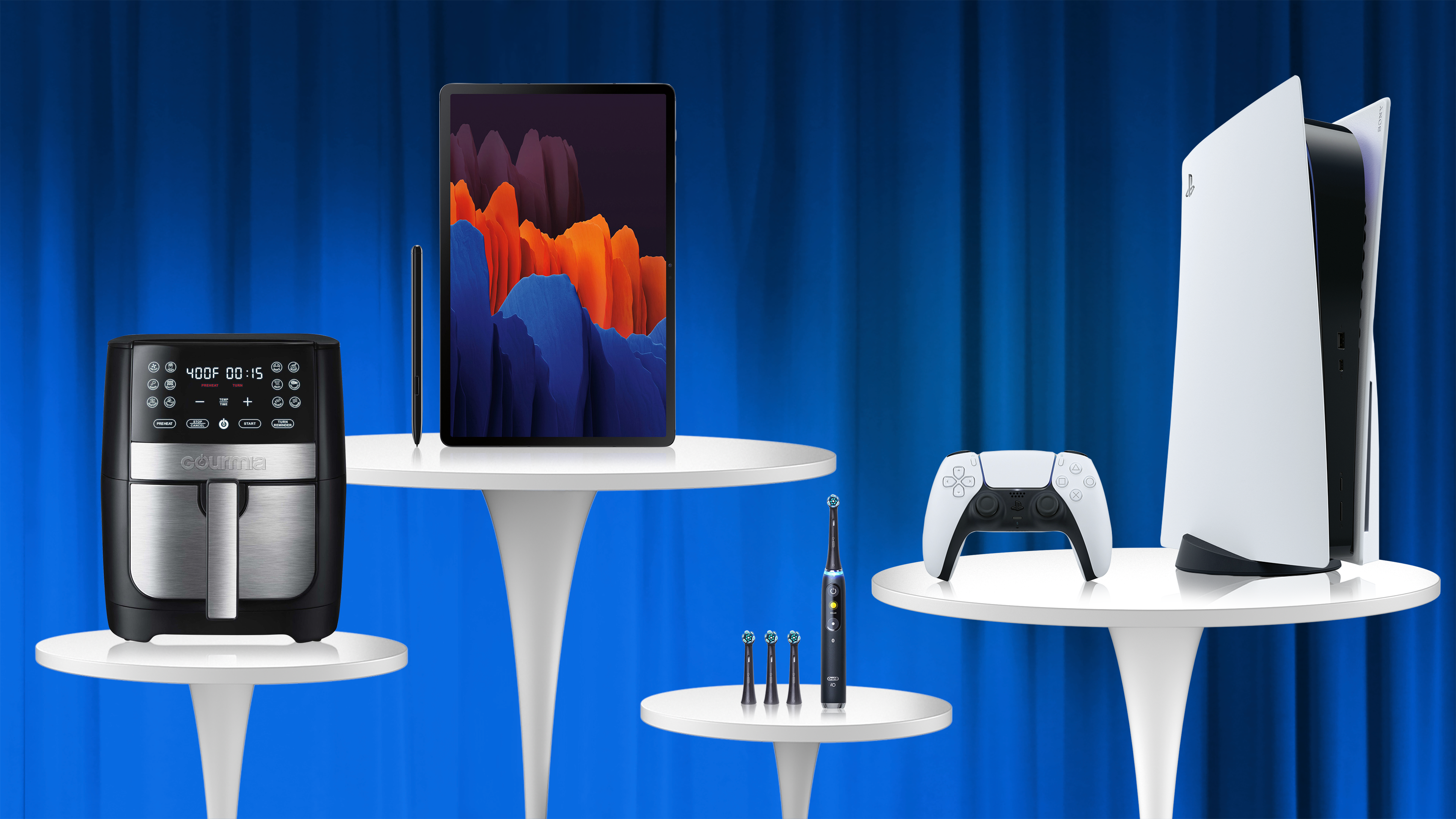 Blue curtain,  white tables with Air Fryer, electric toothbrush, galaxy tablet, playstation 5 and controler