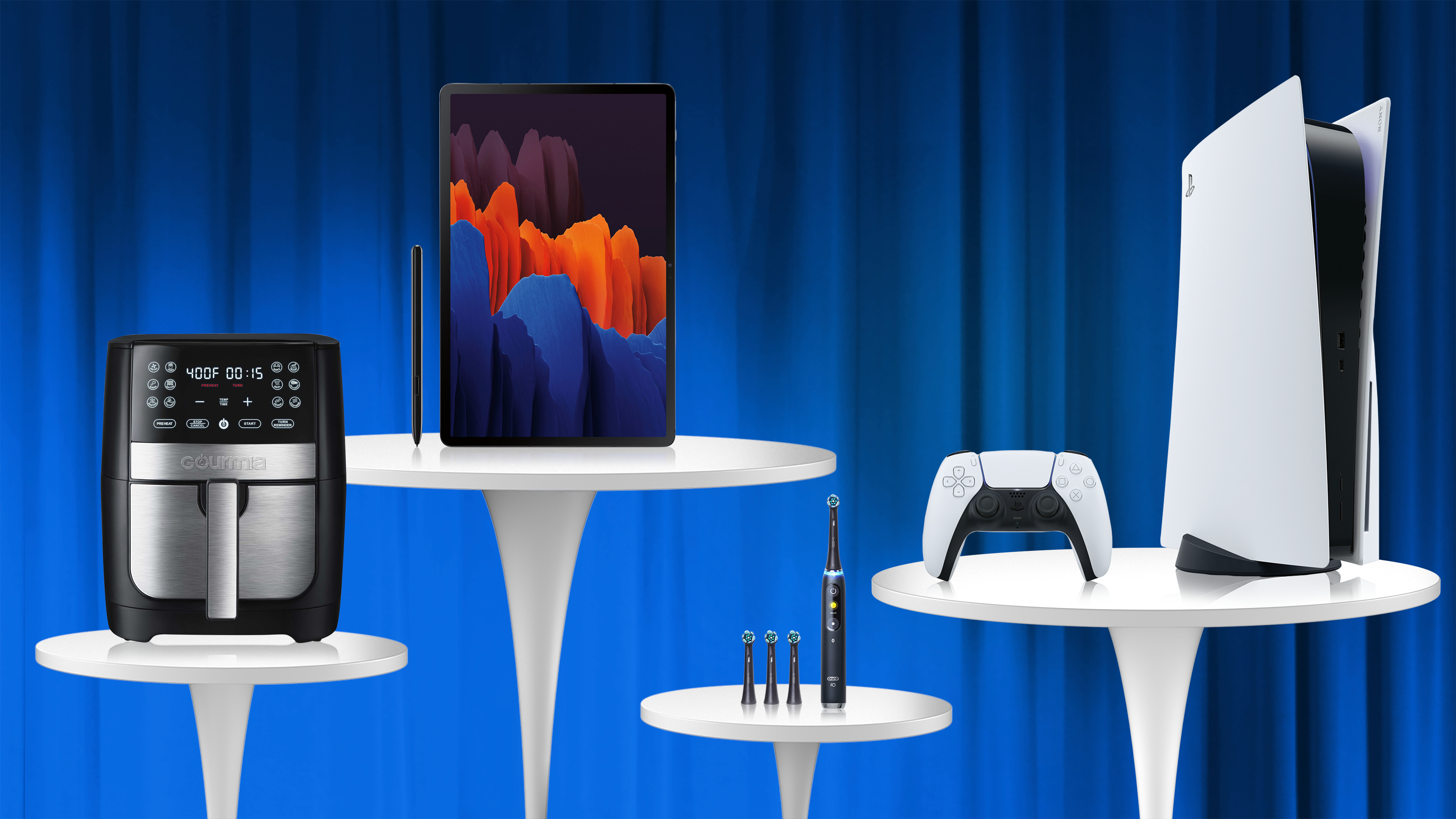 Blue curtain, white tables with Air Fryer, electric toothbrush, galaxy tablet, playstation 5 and controler