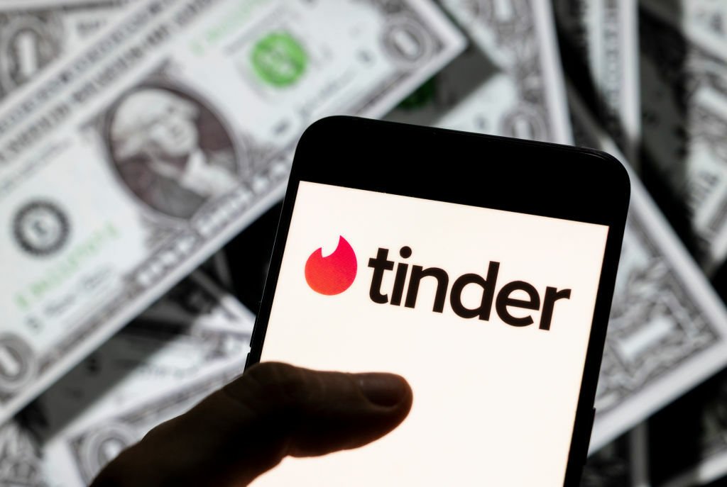 Tinder logo on an Android mobile device screen with the currency of the United States dollar in the background.