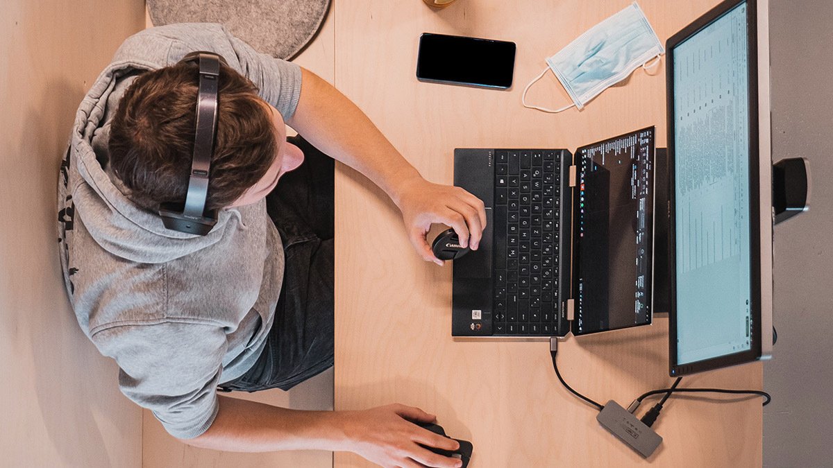 Bird's eye view of person wearing headphones, using laptop with desktop above