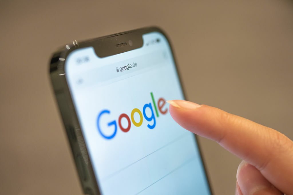 A finger taps a smartphone showing the Google search page.
