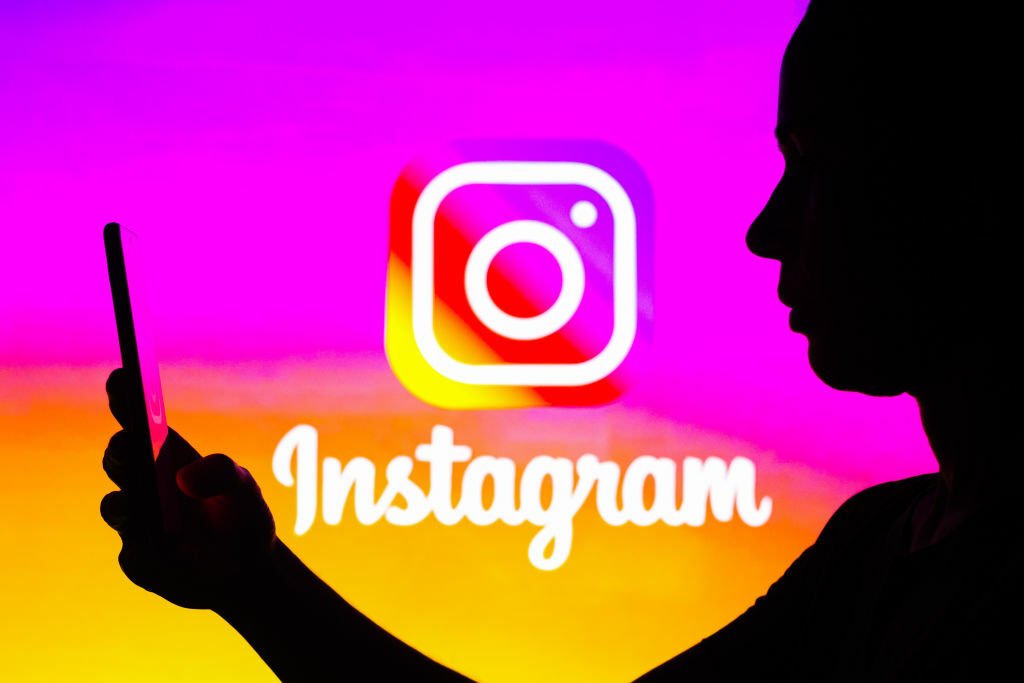  Woman's silhouette is holding a smartphone with an Instagram logo in the background. 