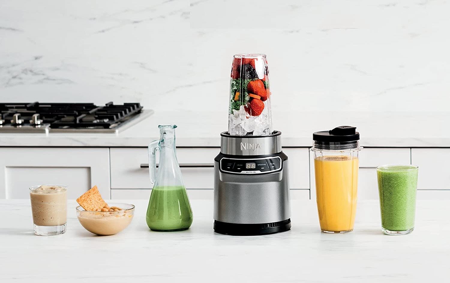 Ninja Nutri Pro personal blender on kitchen countertop next to jars and cups of smoothies, drinks, and sauces