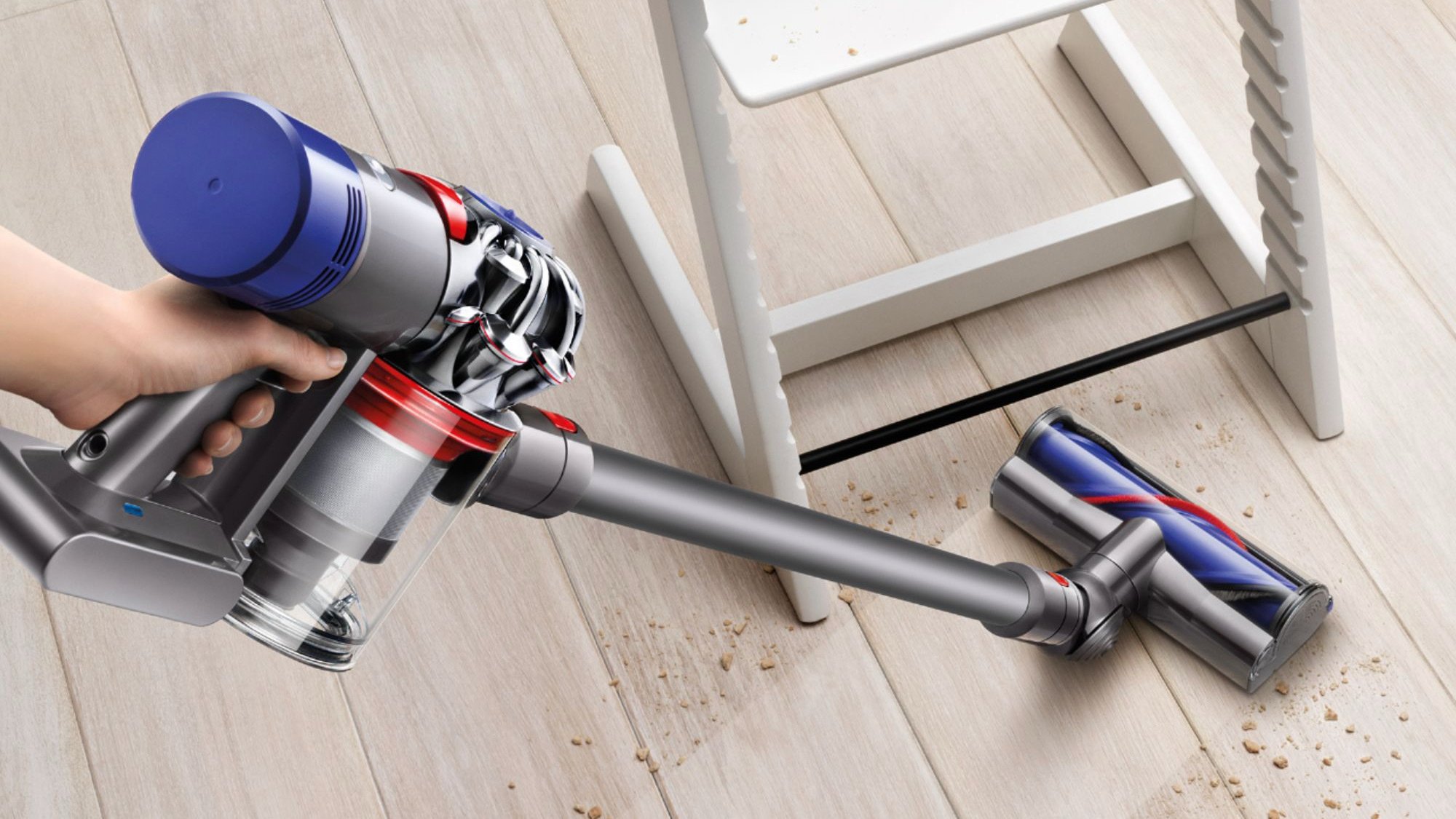 Hand holding purple and grey vacuum cleaning crumbs off floor