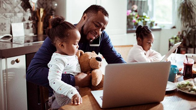 Adult with child smiling at laptop next to other child