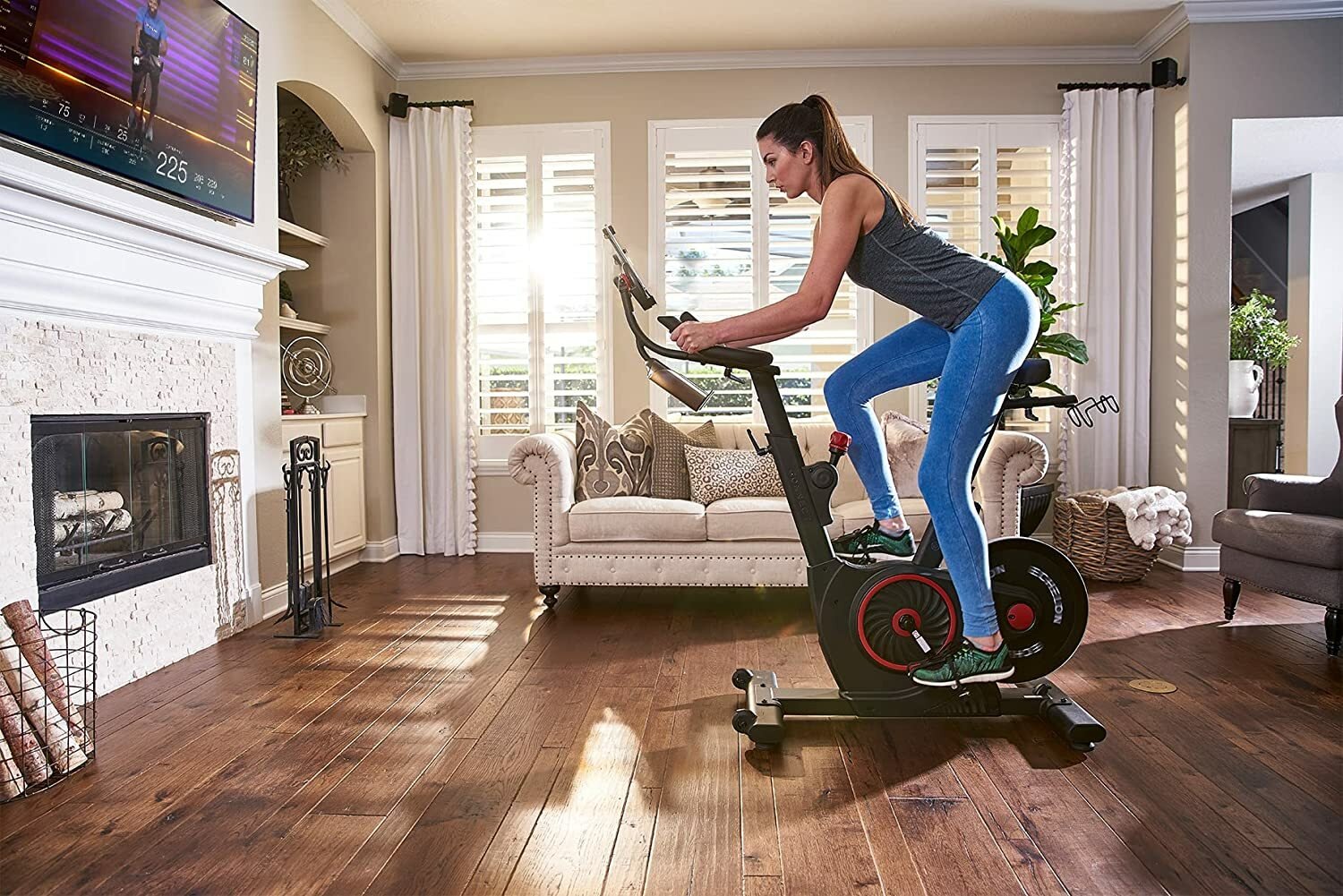 Woman riding Echelon EX5 fitness bike in living room in front of TV playing exercise class.