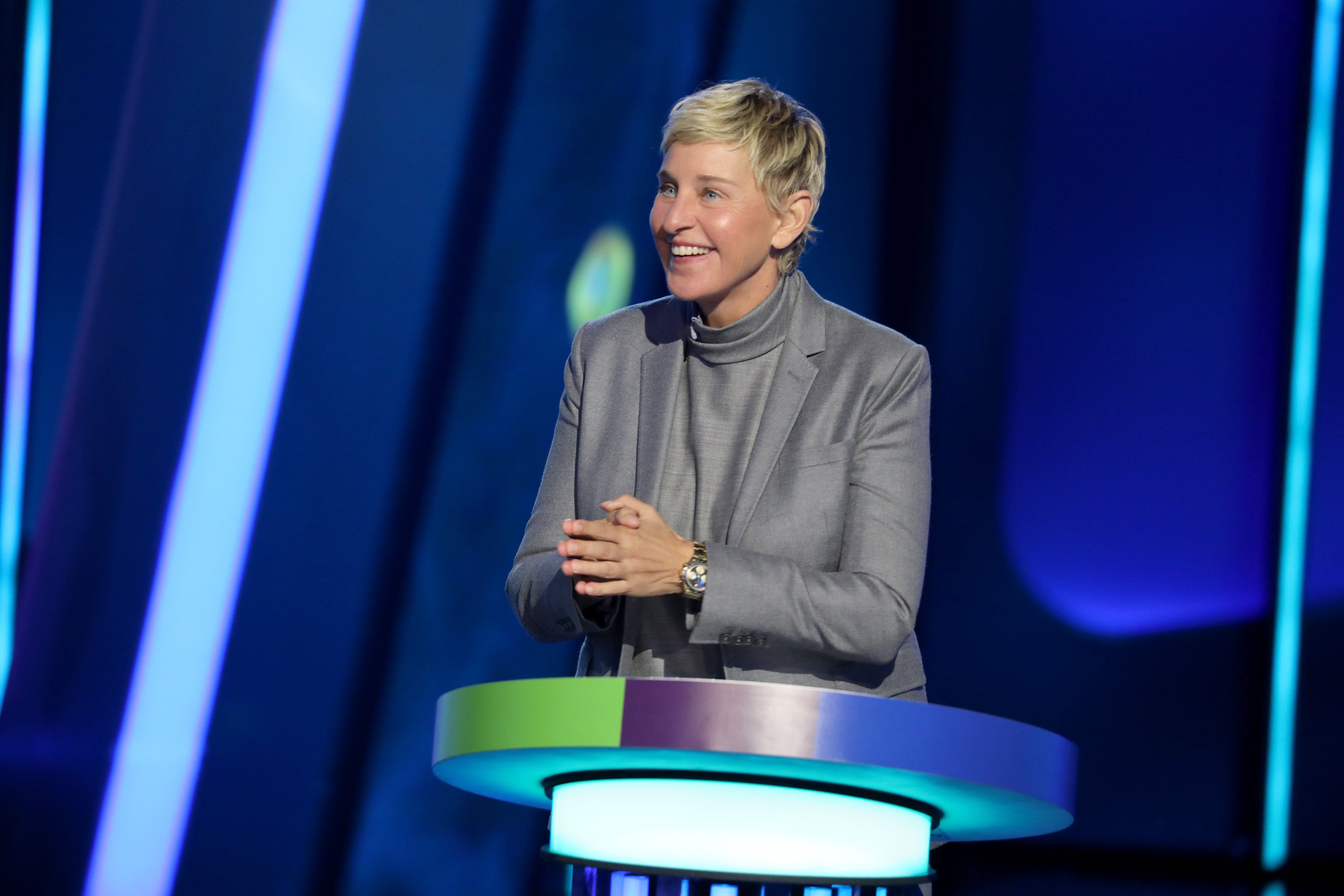 Ellen DeGeneres stands at a gameshow podium.