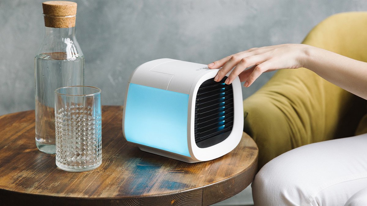 Hand reaching for white air conditioner on wooden bedside table.