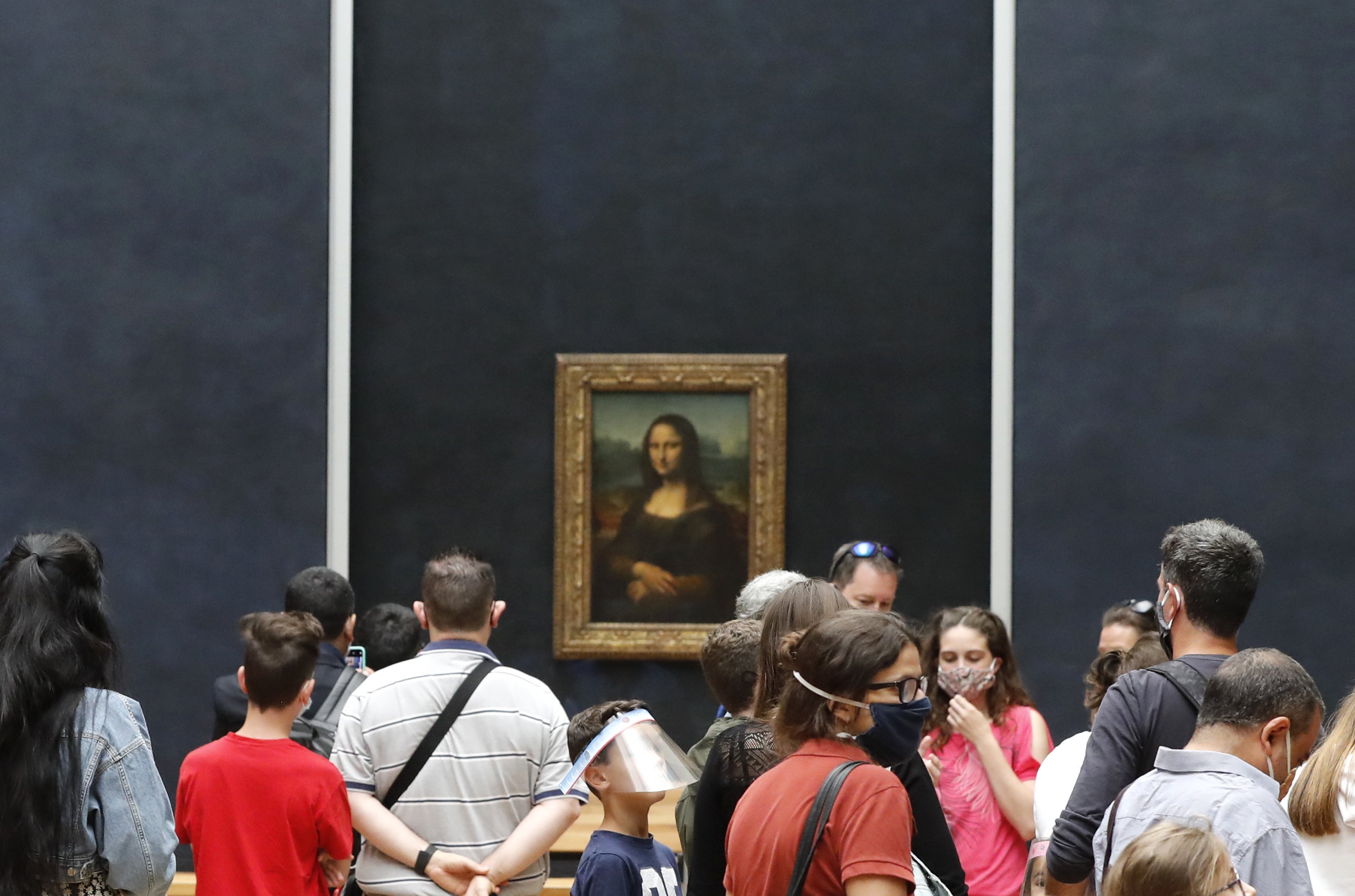 The Mona Lisa painting in a display at the Louvre, surrounded by a crowd of visitors.