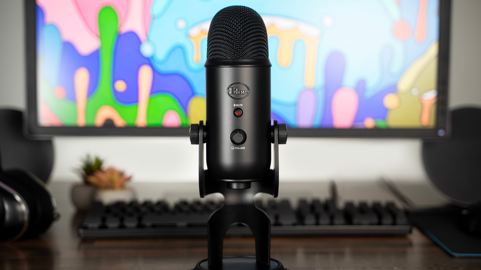 a blue yeti microphone in front of a desktop computer with a bright abstract background