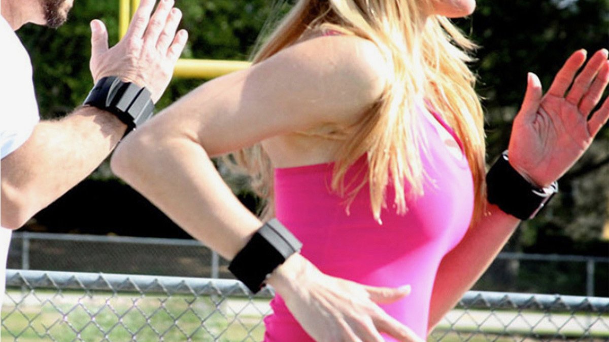 Person's torso running, wearing pink tank top and two black bracelet bands with another arm behind them also wearing black cuff