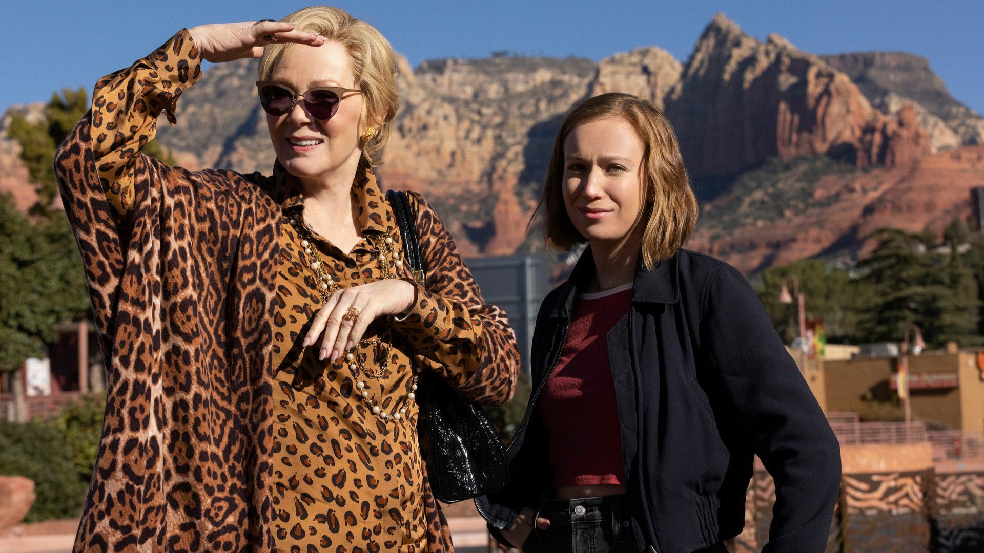 Two women standing in front of red rocky mountains.