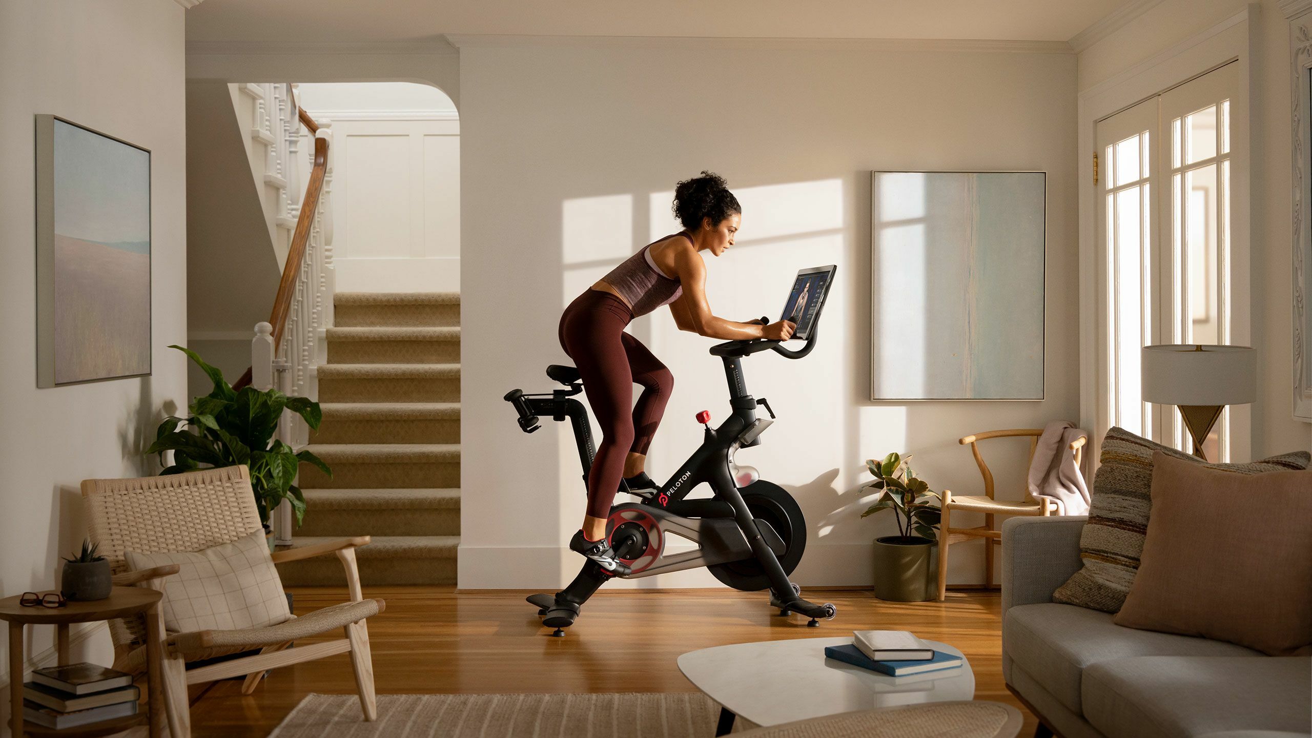 Woman riding a Peloton bike in a bright living room