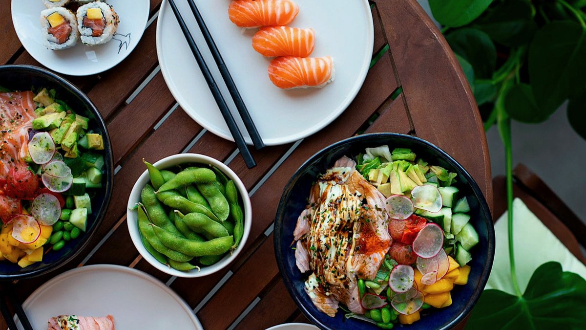 Bowl of edamame, plate of sushi, and bowl of veggies on table