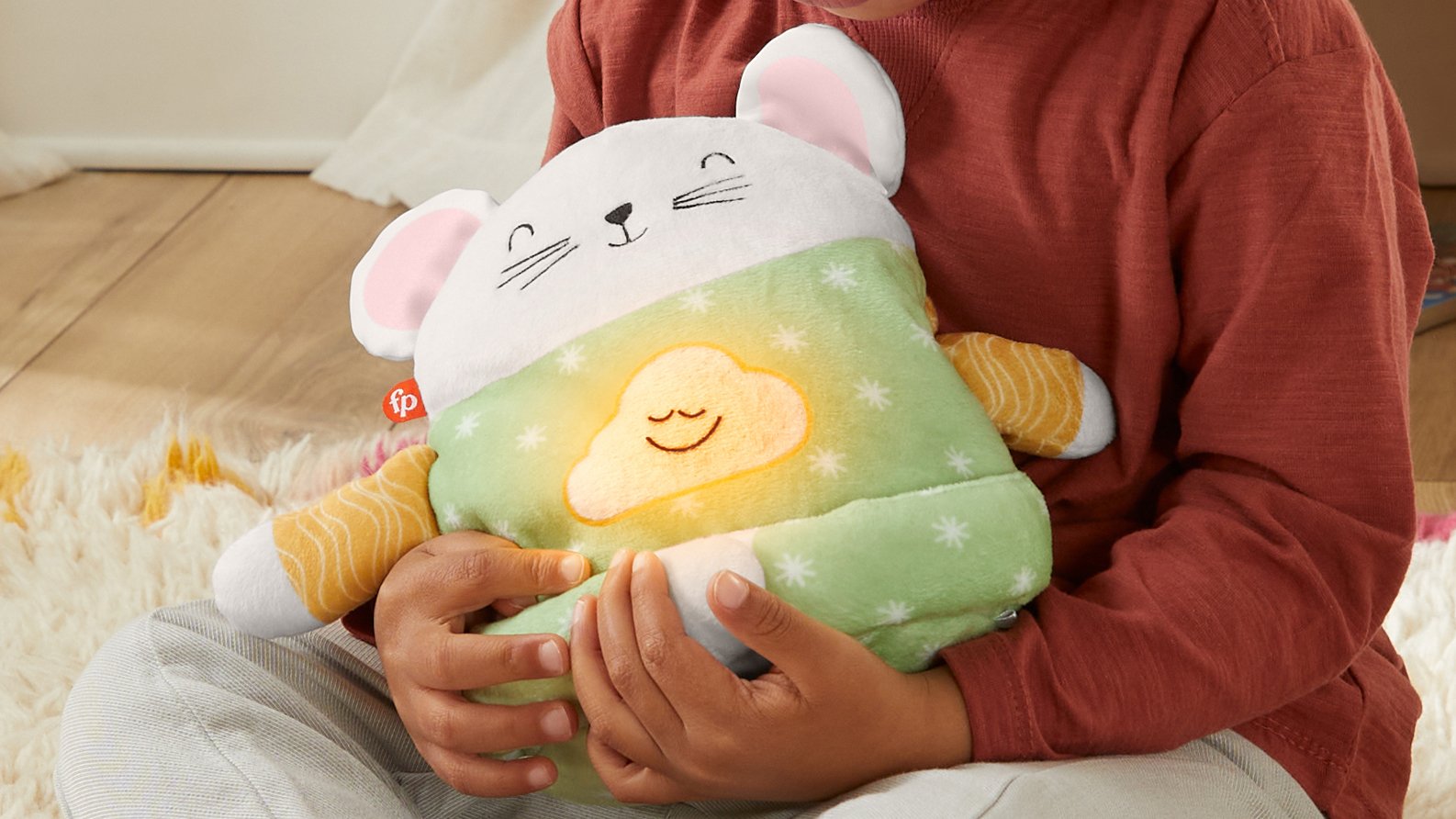 A child holds the Fisher-Price toy Meditation Mouse in their lap.