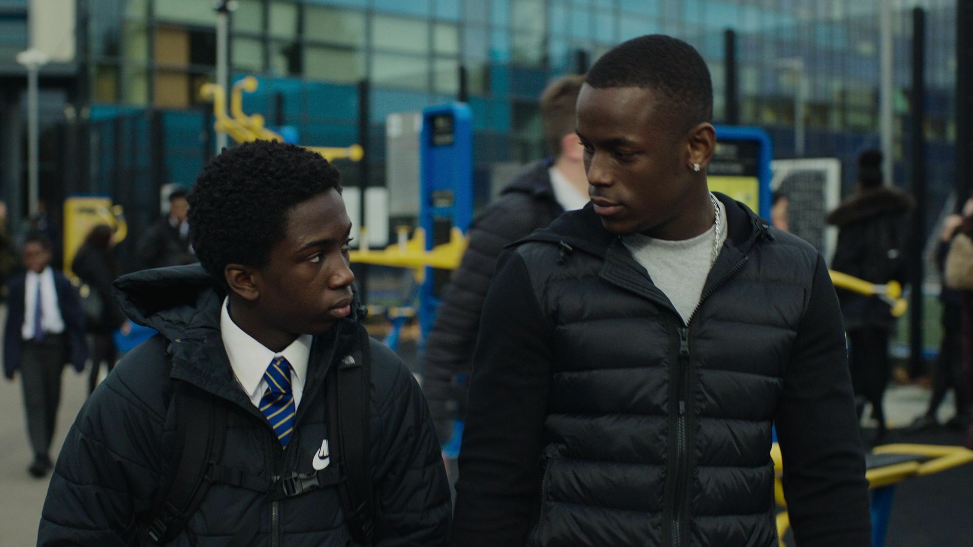 A Black boy in a school uniform looks at another young Black man, from "Top Boy"