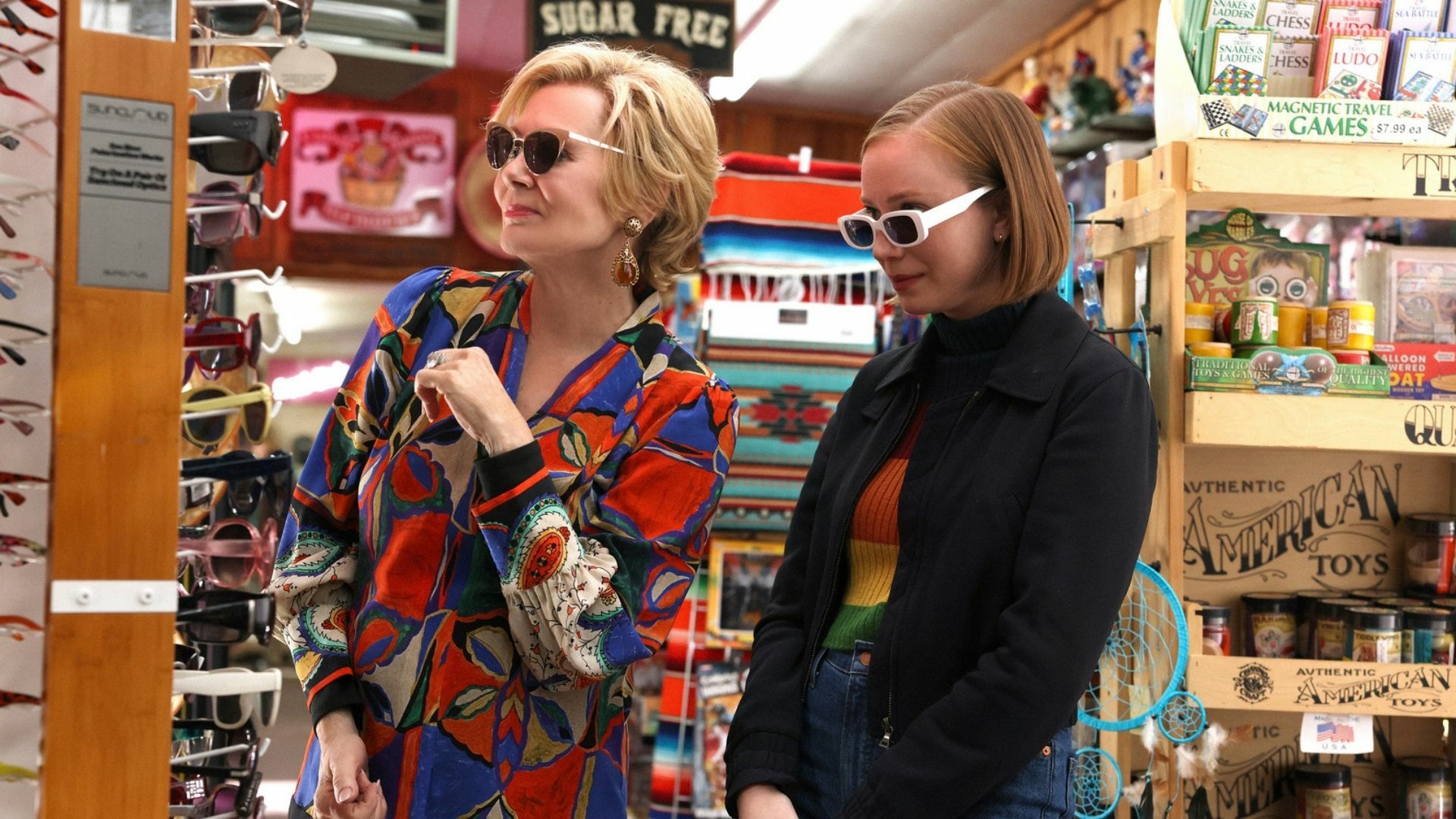 Two women trying on sunglasses in a gas station store.