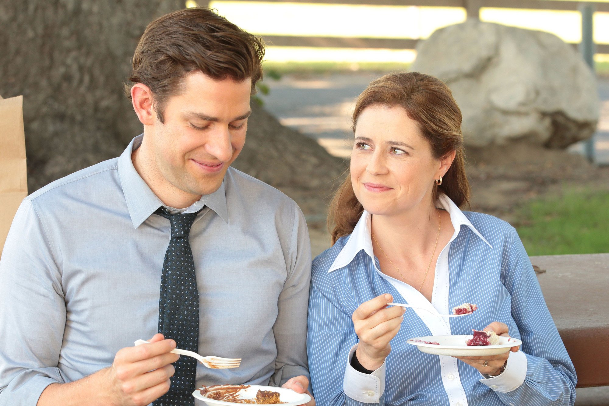 A man (John Krasinski) and a woman (Jenna Fischer) sitting on a bench eating slices of pie.