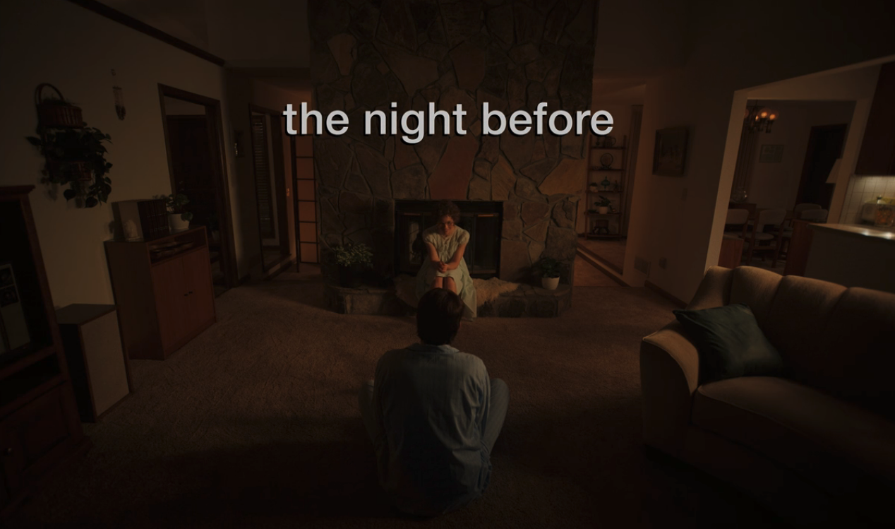 A screenshot from Hulu's "Candy" which shows a woman sitting in front of a fireplace. The screen reads, "the night before."