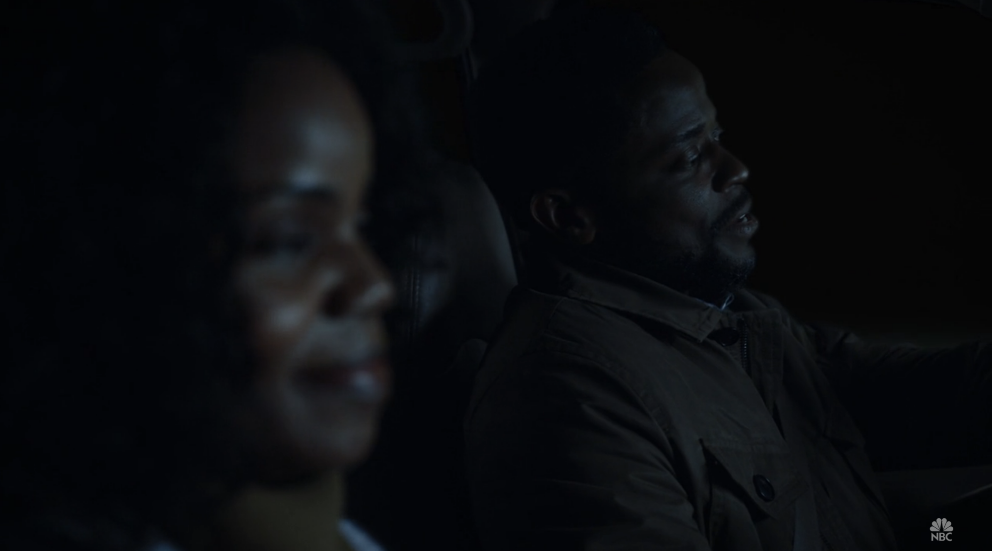 A man and a woman sitting in the driver and passenger seats of a car at night.