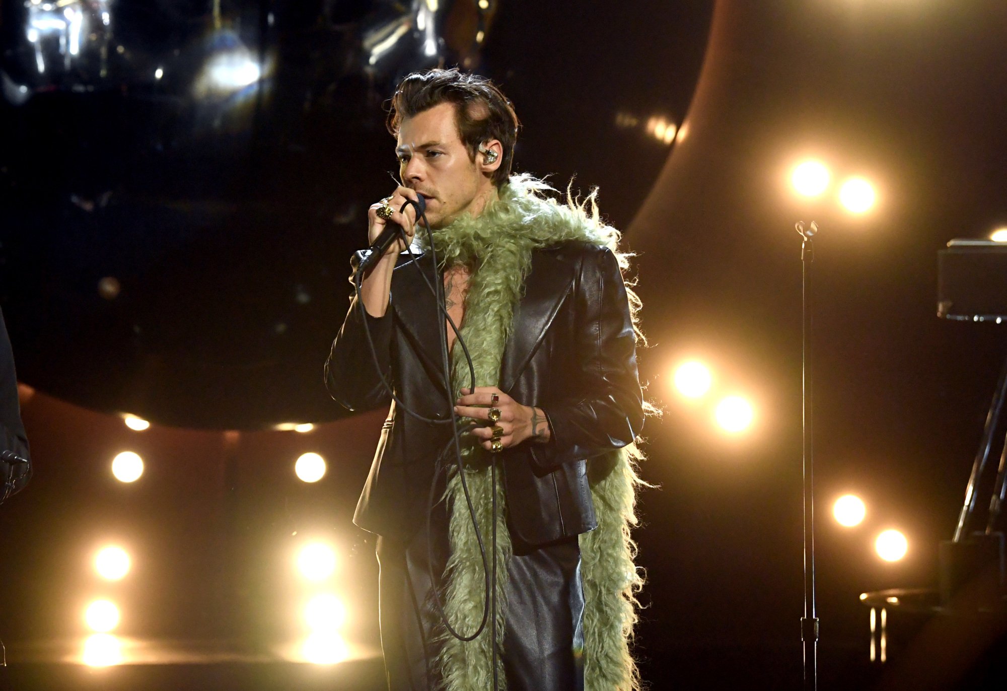 Harry Styles performing at the 2021 Grammys in a black leather suit and fluffy green boa.