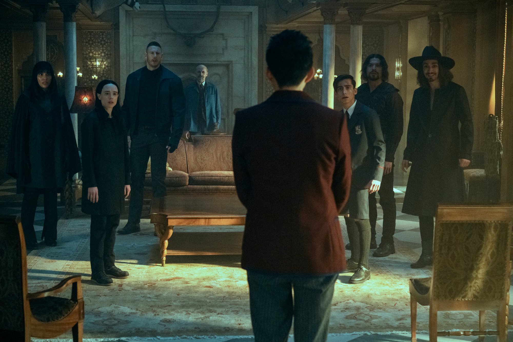 A group of eight people stand in a lavish room in a mansion.