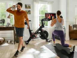 a woman doing strength training in front of a peloton bike+ as a sweaty man walks away from it