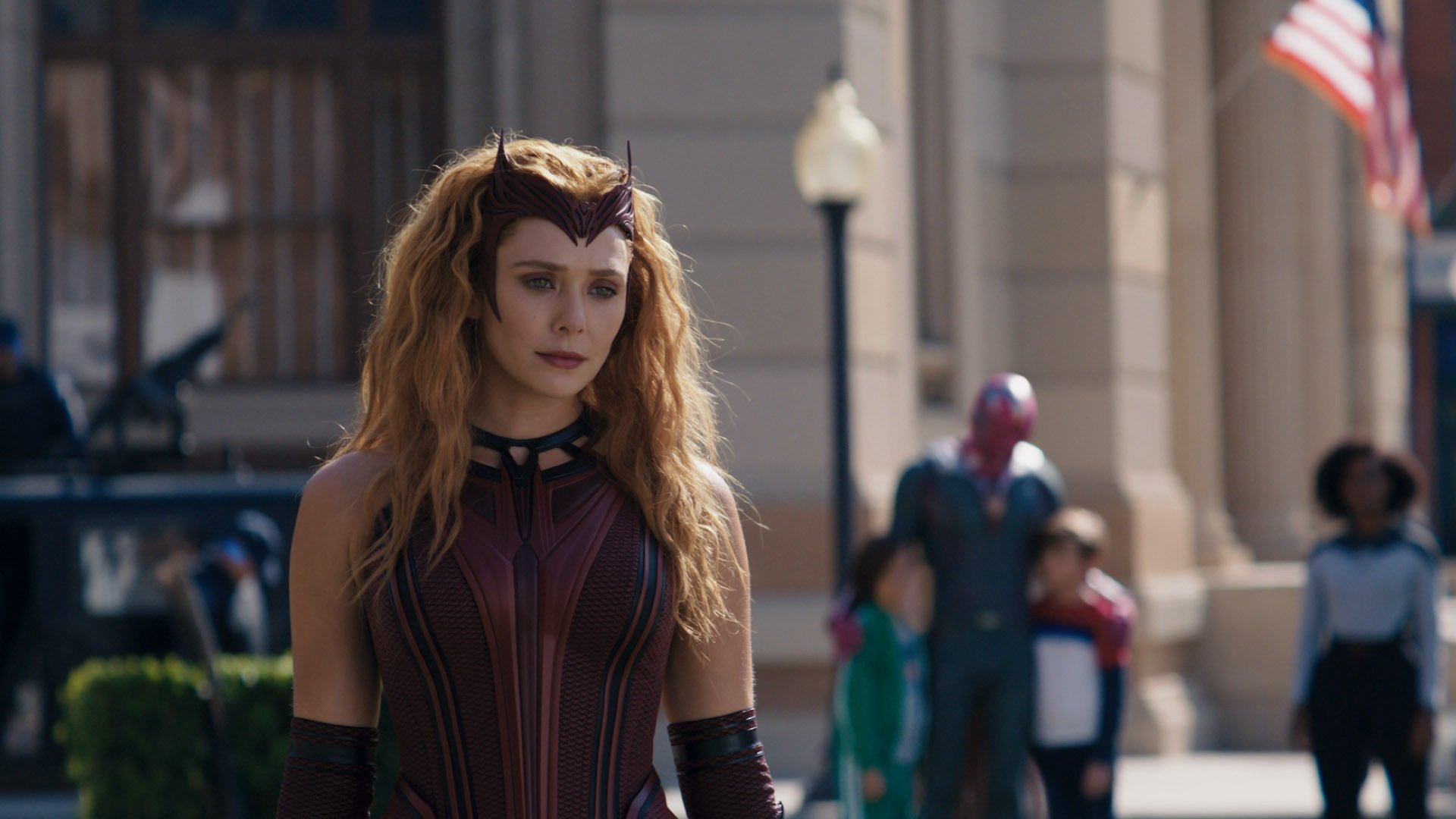 A woman with red-blonde wavy hair wearing a dark red dress and matching headpiece and gloves; Elizabeth Olsen in "WandaVision."