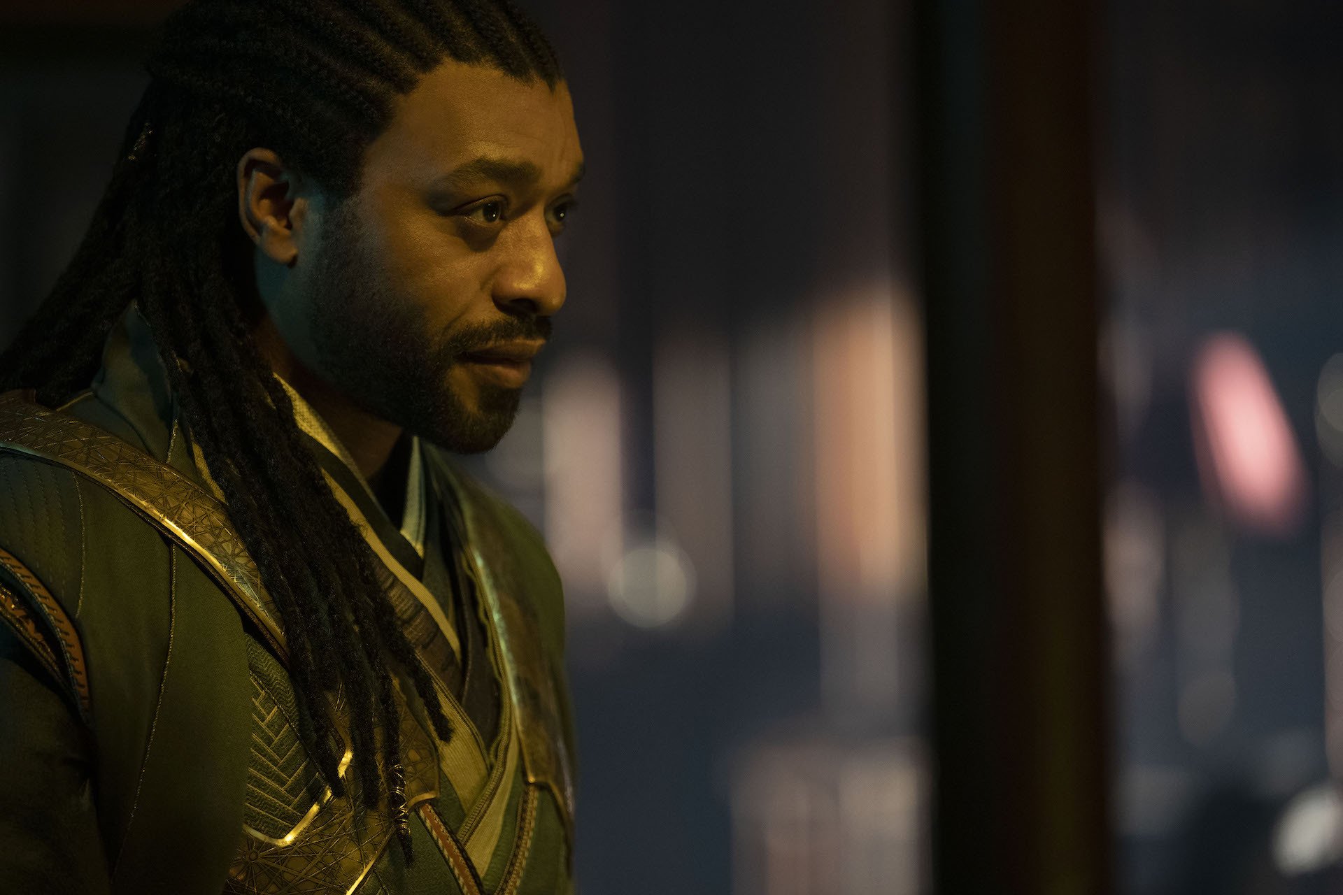 A man in a green robe with long locs staring into the distance.