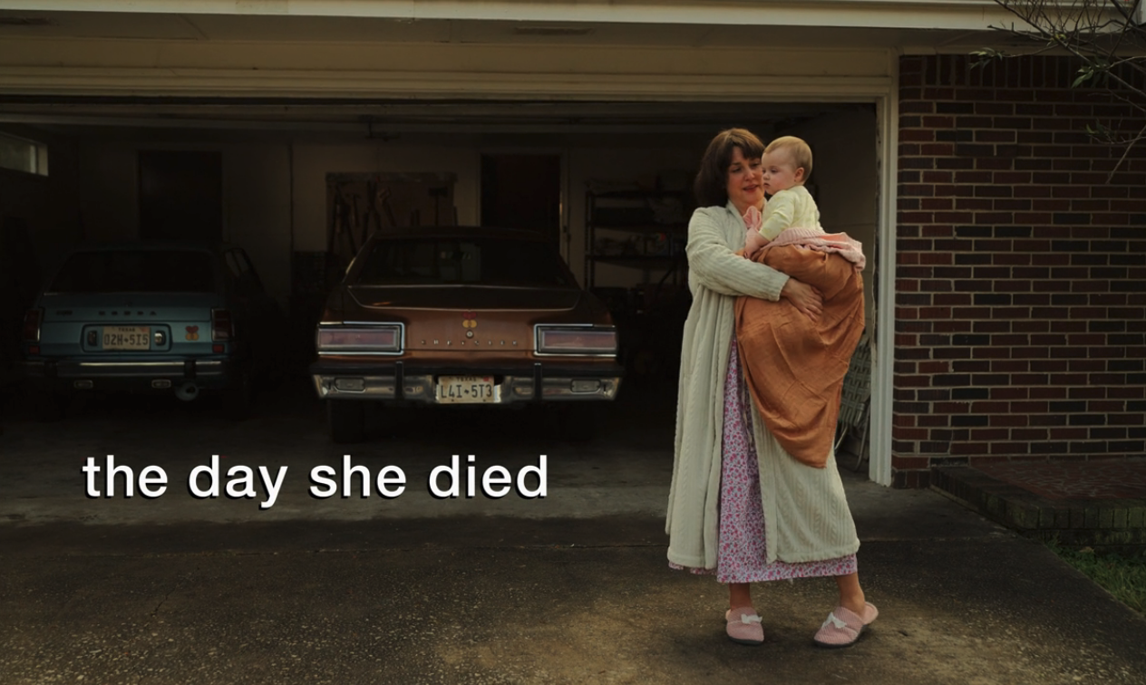 A screenshot from Hulu's "Candy" which reads, "the day she died." A woman is pictured standing in a driveway, holding a baby.