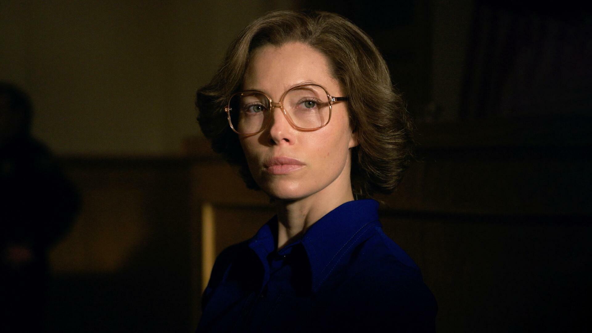 A woman in a blue dress and large glasses.