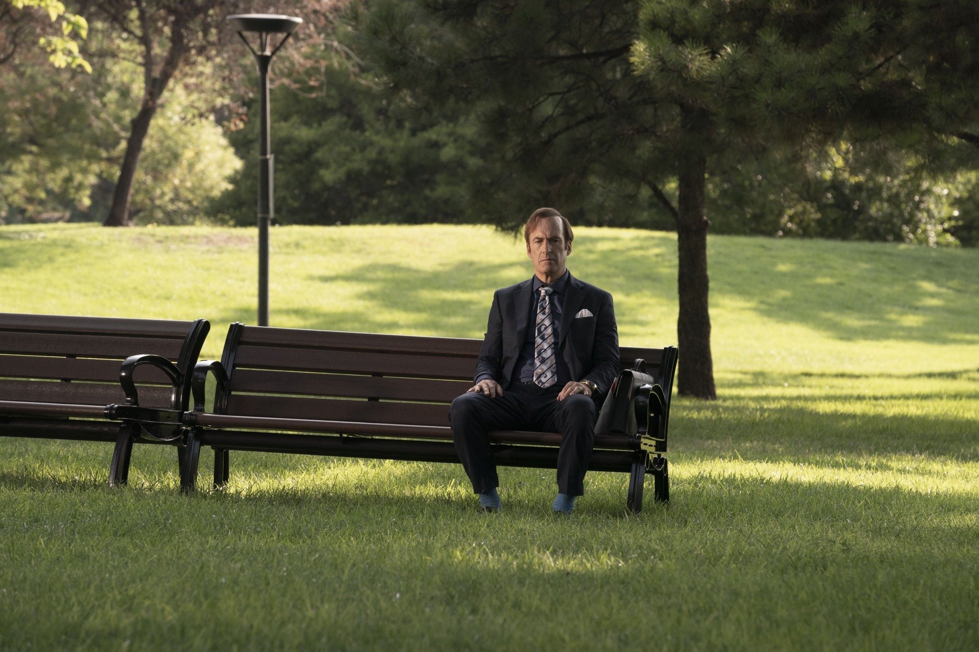 A man (Bob Odenkirk as Jimmy McGill) sitting outside on a park bench.