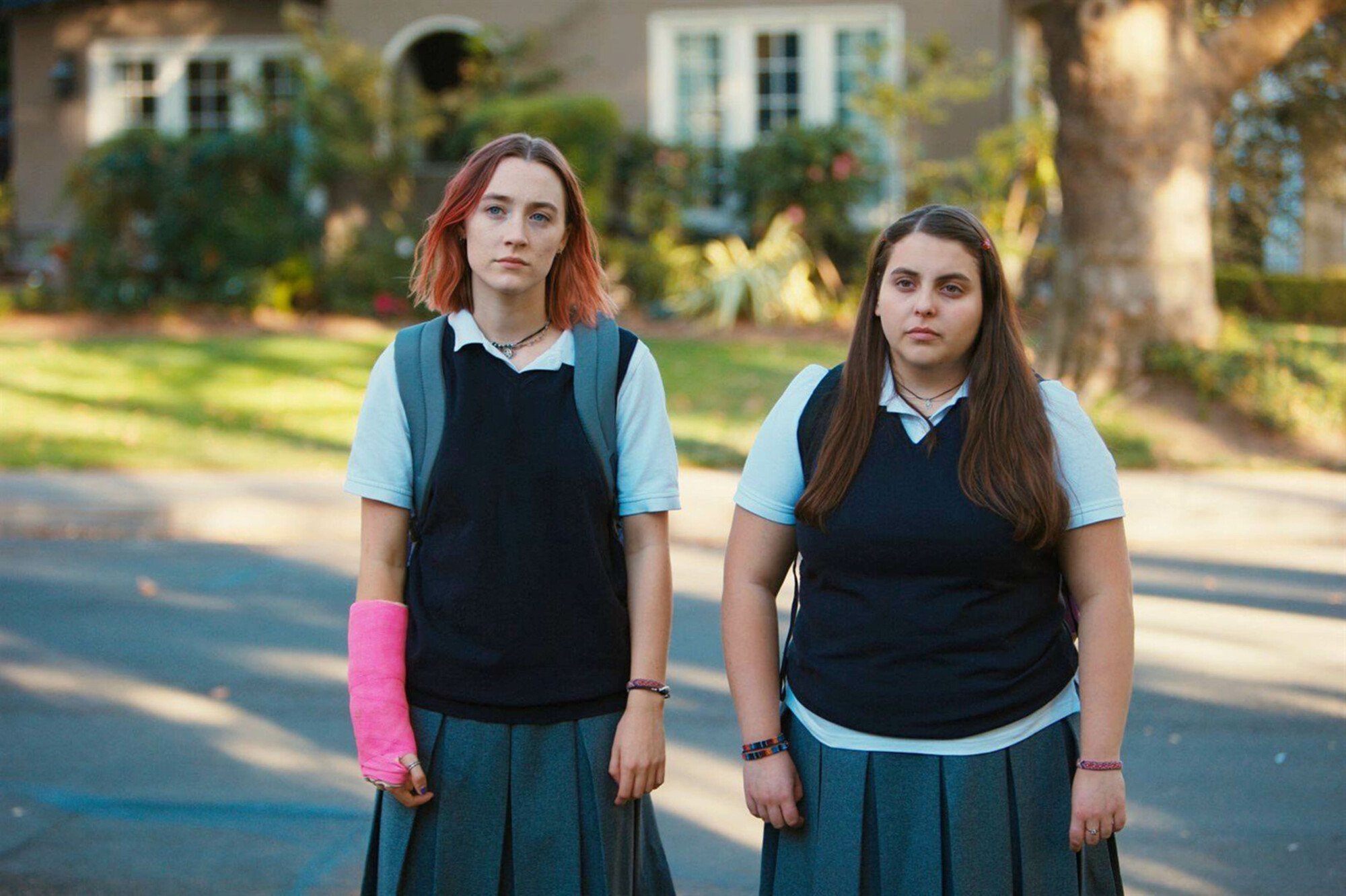 Two young women in school uniforms stand in the street.